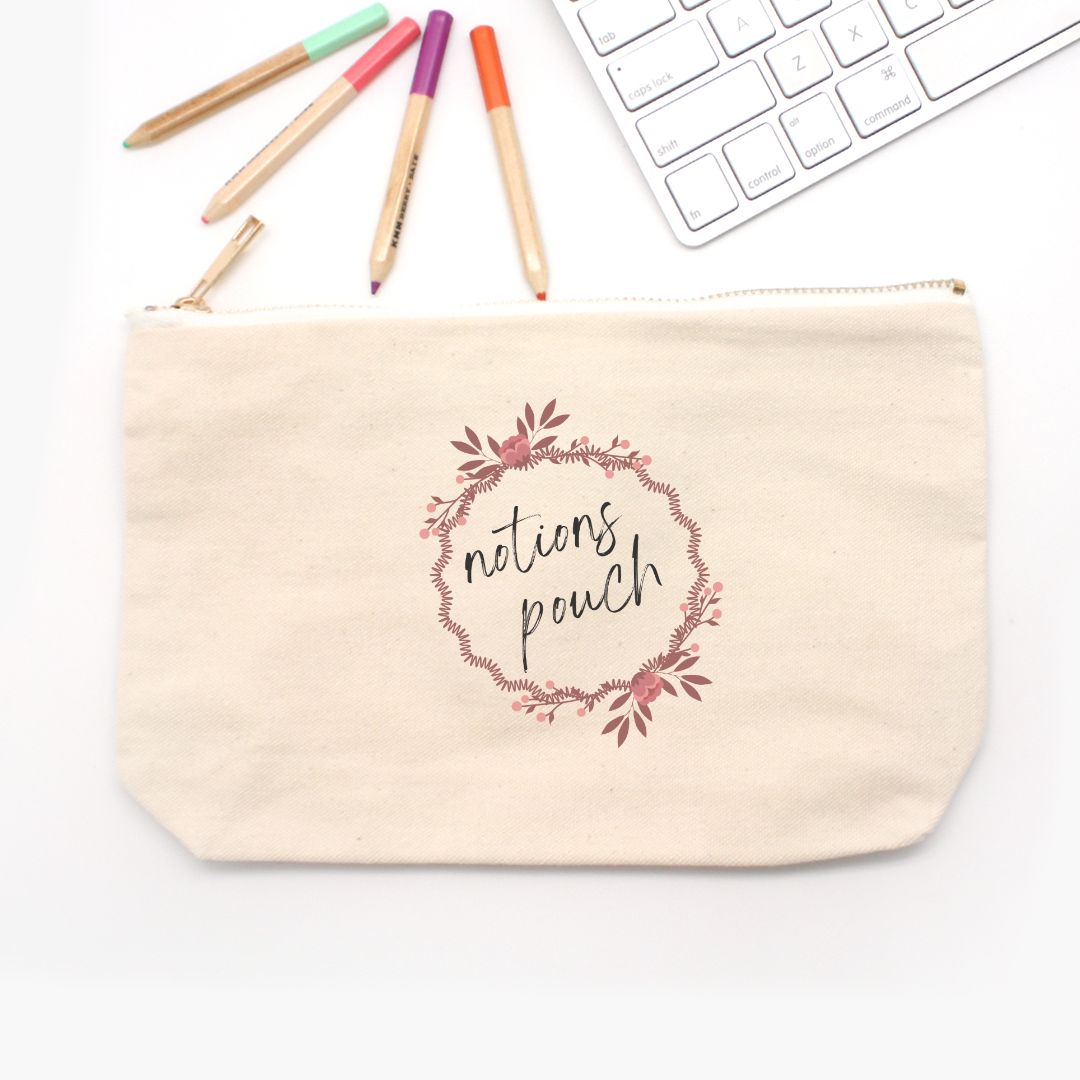 A beige canvas pencil bag with a floral design and the text 'nations pouch' printed on the front. It features a zipper closure. The pouch is on a white desk next to a white keyboard and markers.