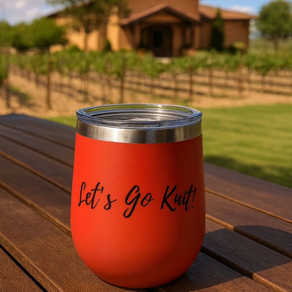 Red wine tumbler with 'Let's Go Knit!' text on a wooden table in front of a vineyard.