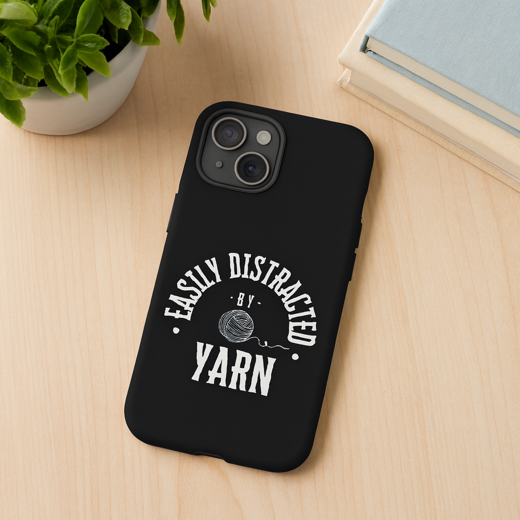 Black phone case with 'Easily Distracted by Yarn' text on a wooden surface