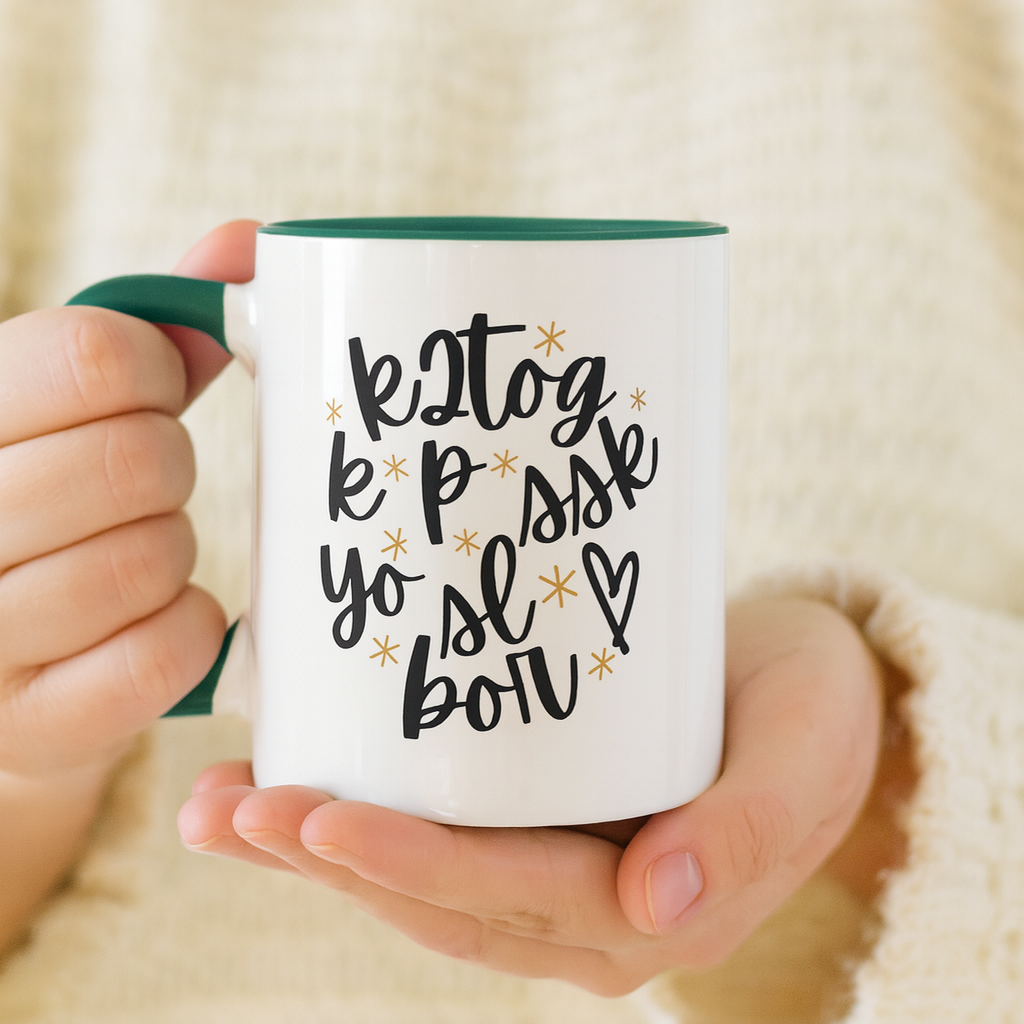 Person holding a mug with decorative text and design. The person is wearing a cream color sweater. The photo is bright and airy. Knitting Enthusiast Mug for Yarn Lovers