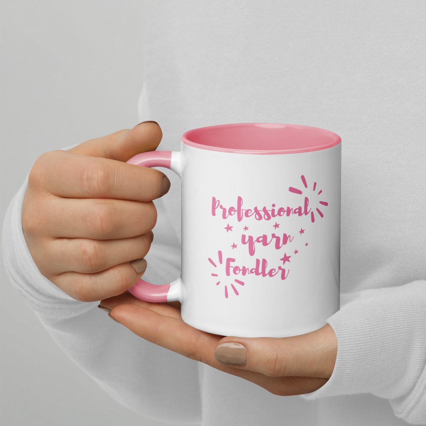 White mug with pink interior and handle, held by a hand, featuring text 'Professional yarn fonder'.