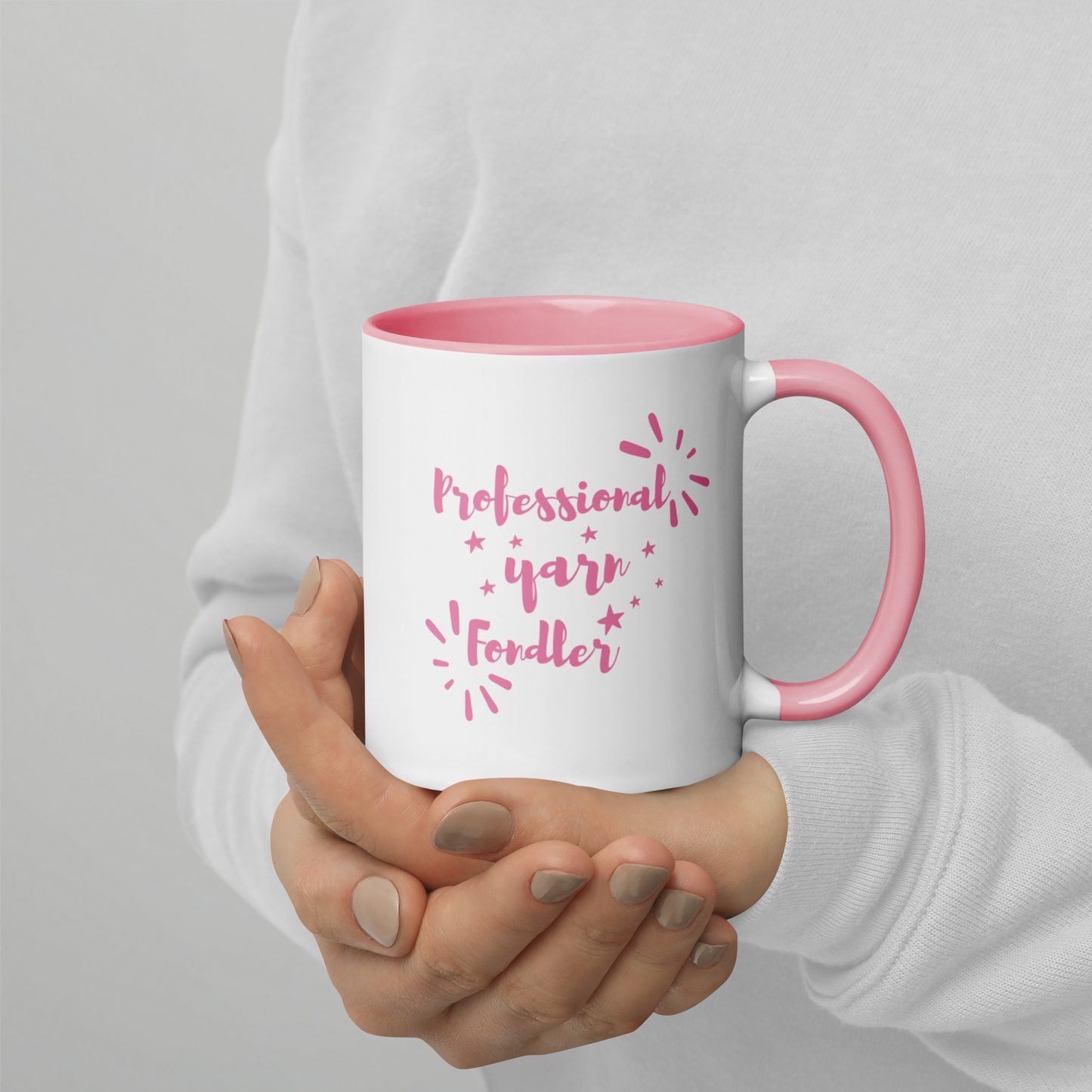 White mug with pink interior and handle, held by a person, featuring the text 'Professional yarn fonder' on a gray background.