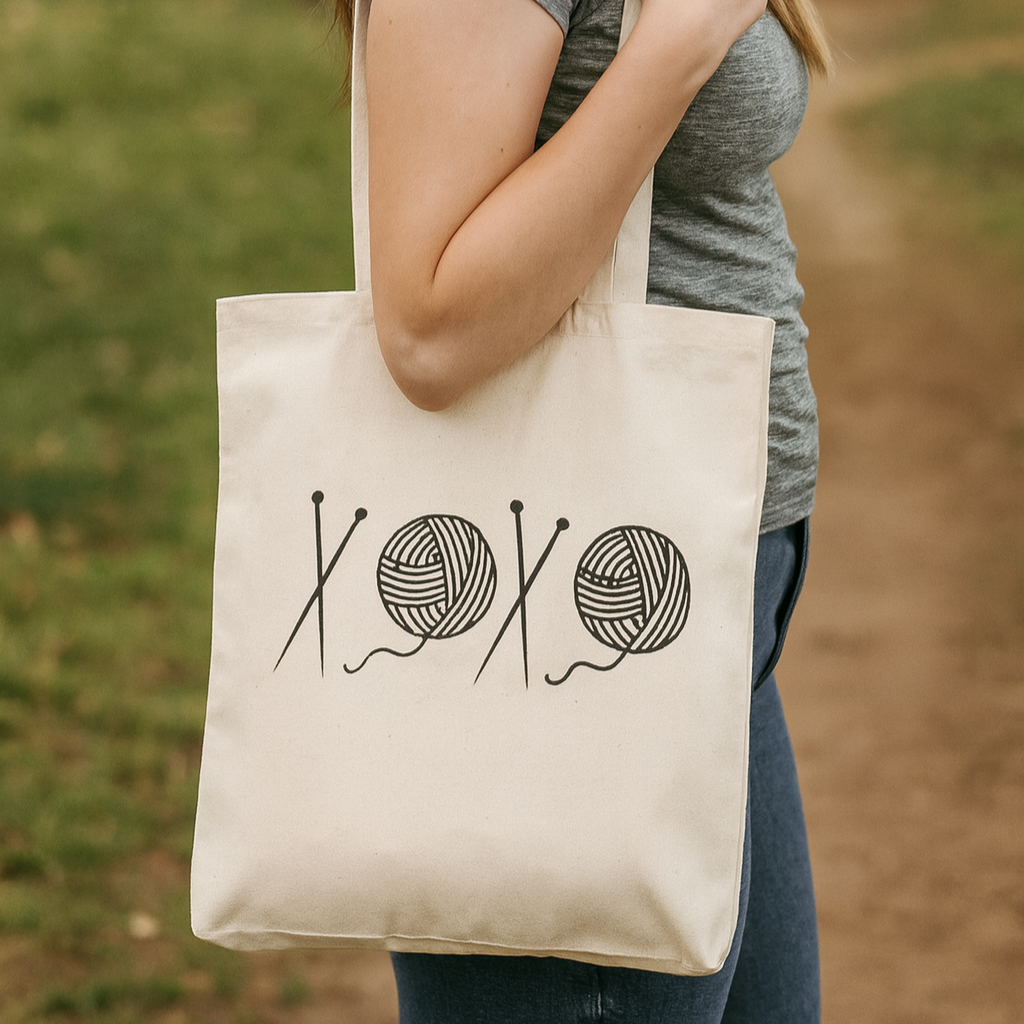 Person holding a tote bag with yarn and knitting needles design outdoors.
