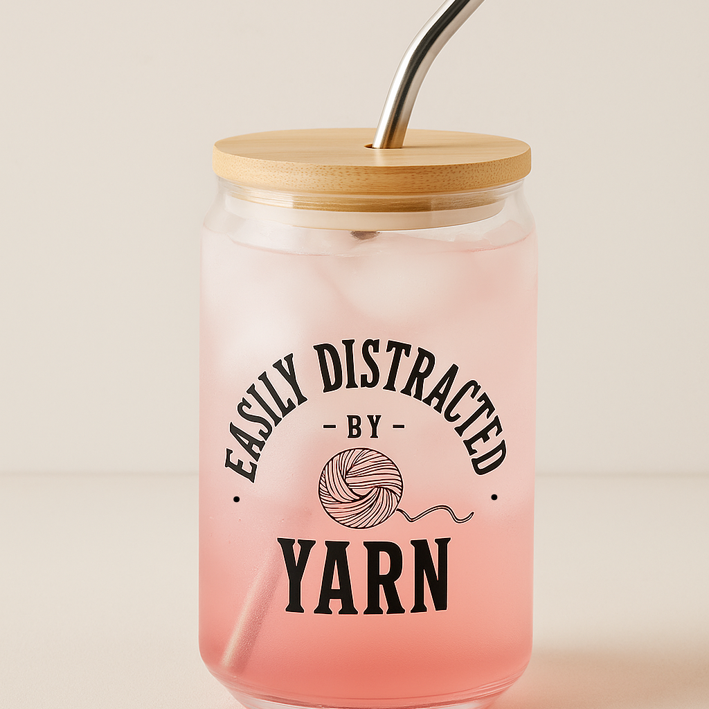 Pink tumbler with wooden lid and metal straw featuring 'Easily Distracted by Yarn' text.