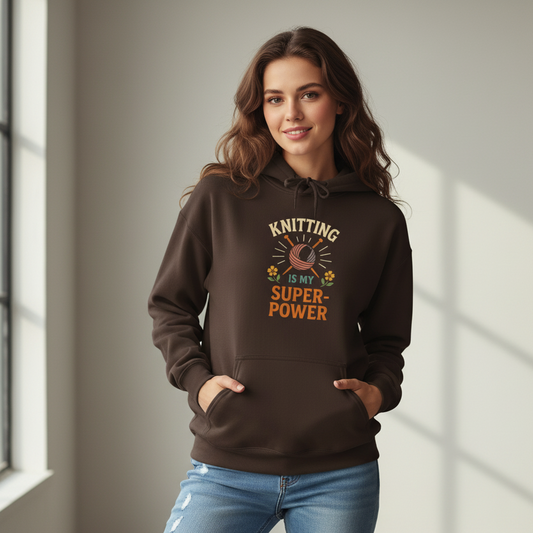 A woman wearing a chocolate brown hoodie sweatshirt that says "Knitting Is My Super-Power".  The letters are in warm tones, with a drawing of knitting needles and yarn.  