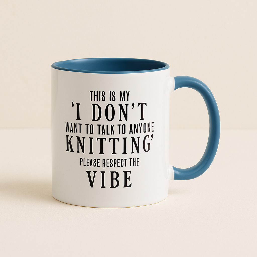 A white ceramic mug with a light blue handle and inner lining, featuring bold black text that reads, "This is my 'I don't want to talk to anyone knitting' please respect the vibe." The mug is displayed against a neutral beige background, emphasizing its playful and humorous design. Perfect for knitting enthusiasts who enjoy their quiet time.