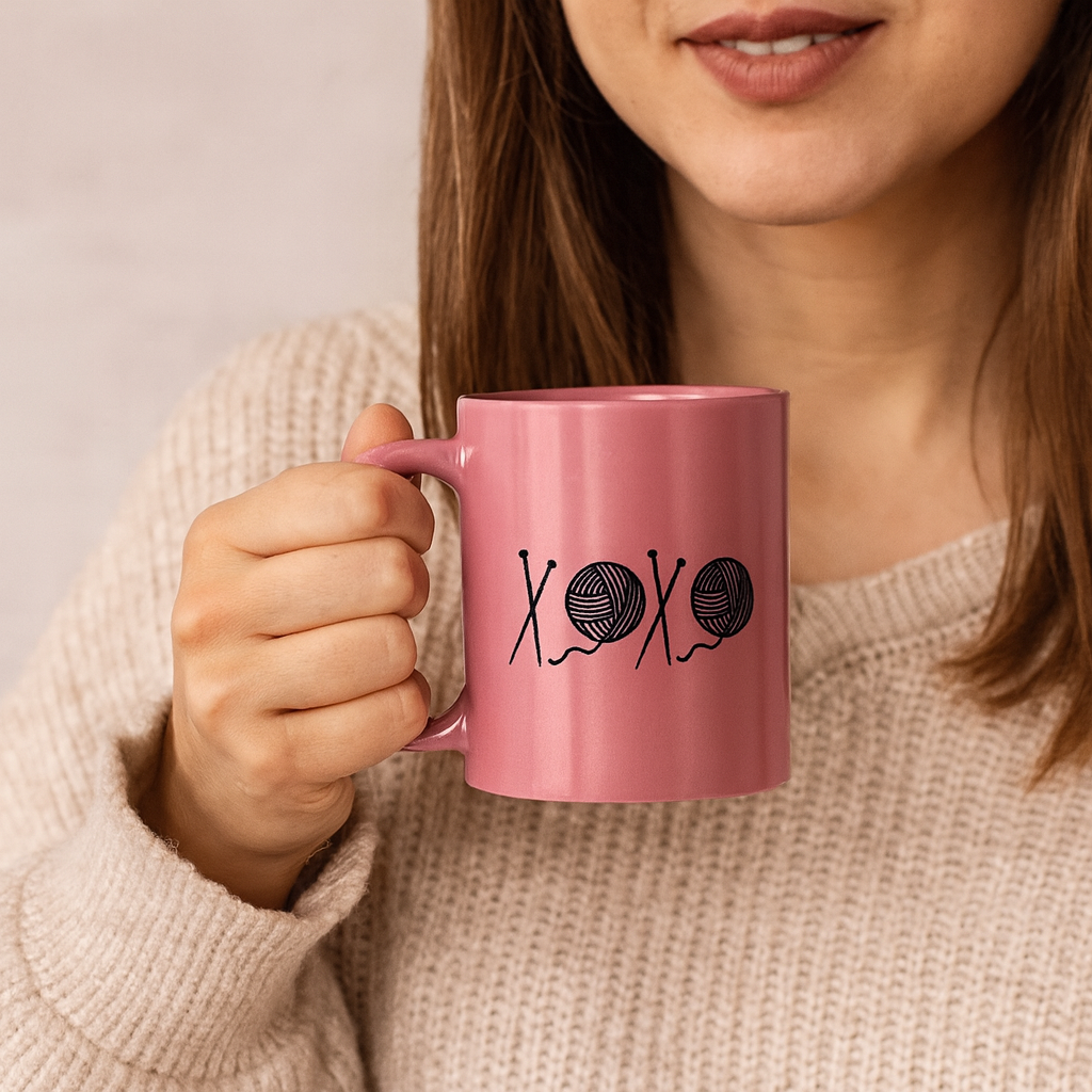 Person holding a pink mug with yarn and heart design